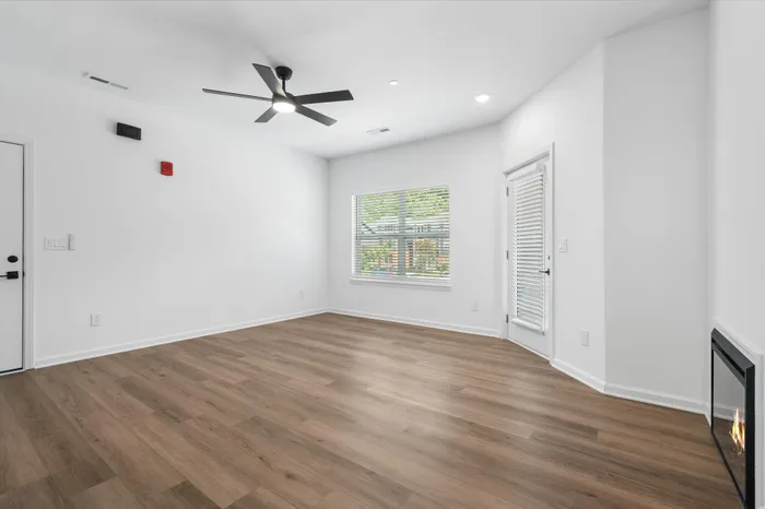 Bright and airy living room with elegant wood flooring, modern ceiling fan, and cozy fireplace, offering a warm and inviting atmosphere.