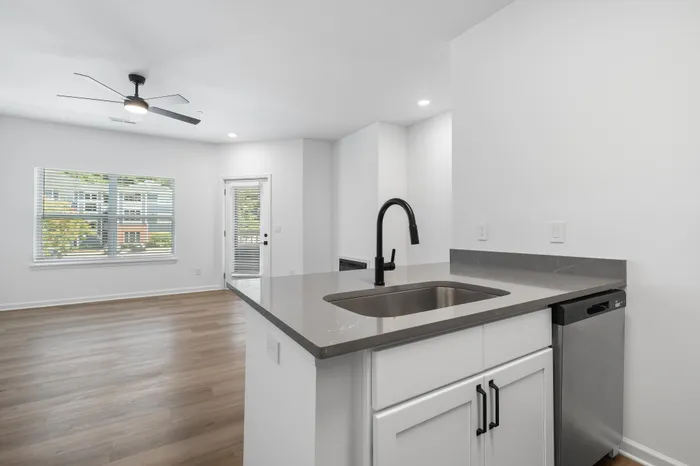Bright and modern kitchen with sleek countertops and high-end fixtures, seamlessly opening into a sunlit living area with large windows and stylish hardwood floors.