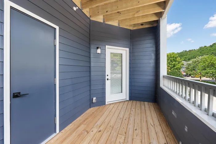 Elegant and inviting balcony with modern blue siding and wood flooring, offering serene views of lush greenery.