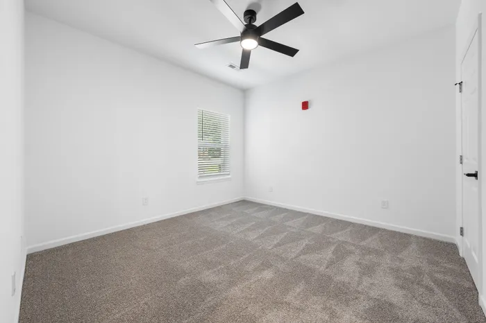 Bright, modern bedroom with plush carpet and sleek ceiling fan in a stylish apartment.