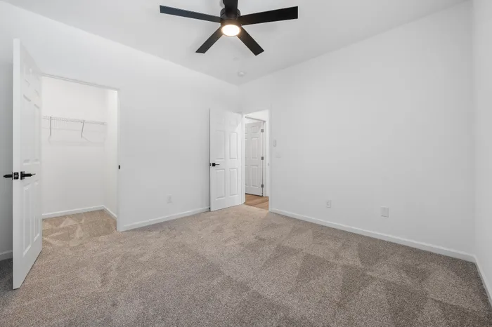 Bright bedroom with plush carpet, sleek ceiling fan, and spacious walk-in closet offering modern comfort.