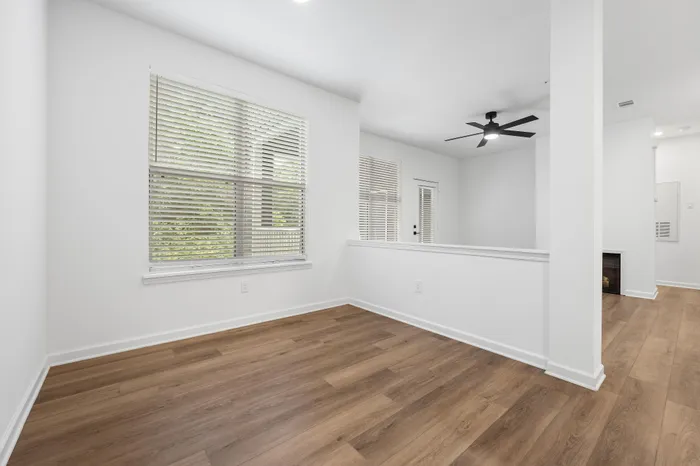 Bright and inviting apartment interior featuring wide plank hardwood floors, large windows with blinds, and a modern ceiling fan for stylish comfort.