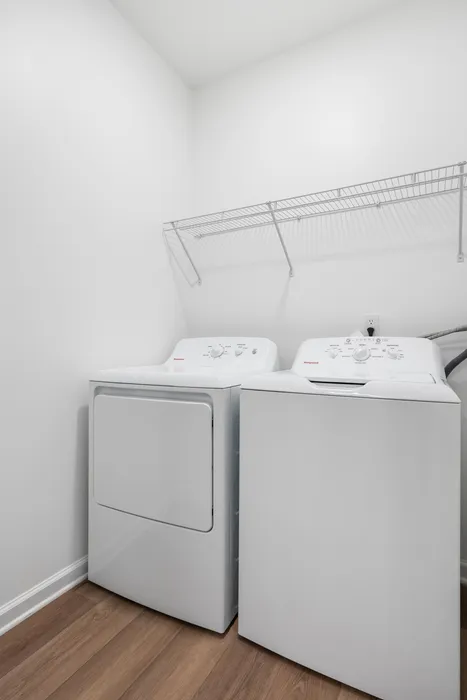 Contemporary laundry room with sleek washer and dryer on elegant hardwood floors, enhanced by a practical overhead wire rack.