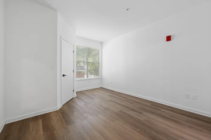 Bright and airy room with elegant wood flooring, large window, and minimalist design in a spacious apartment.