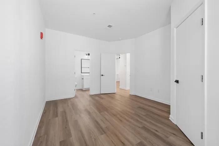 Bright, modern interior room with sleek wood flooring, white walls, and multiple doorways leading to a bathroom and additional space.
