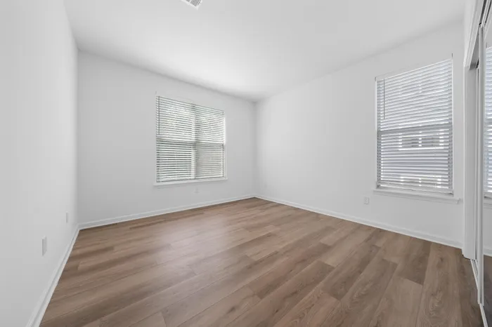 Bright, spacious room with elegant wooden flooring and ample natural light from large windows, perfect for a cozy bedroom setup.
