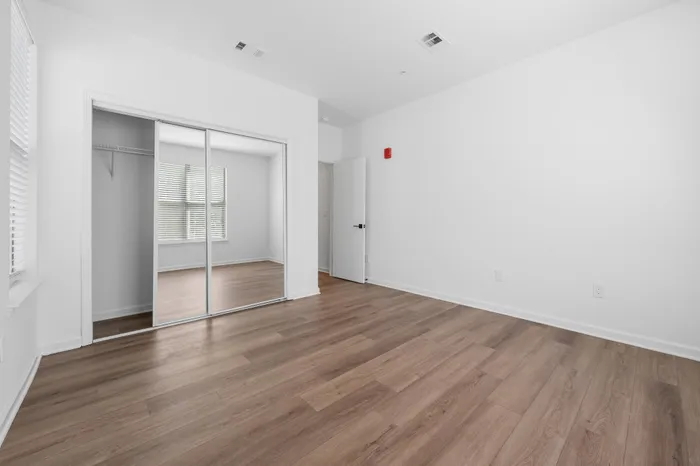 Bright and airy room with sleek wooden floors, large mirrored closets, and ample natural light creating a modern, inviting atmosphere.