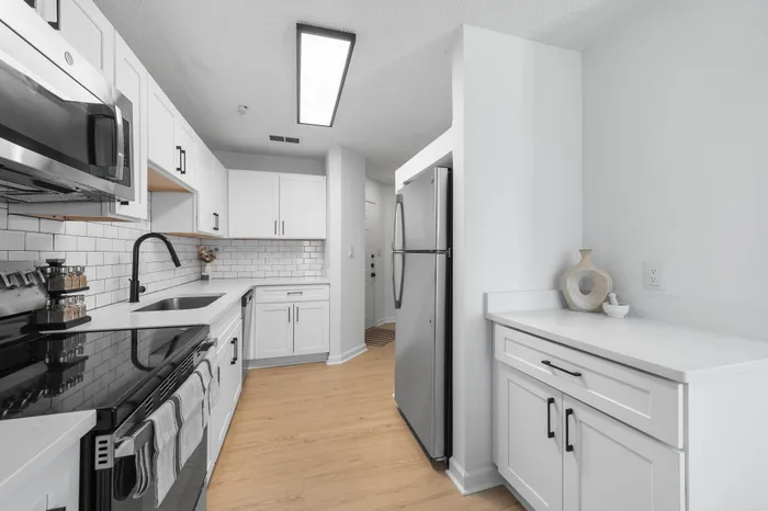 Modern kitchen with sleek stainless steel appliances, white cabinetry, and elegant subway tile backsplash on light wood flooring.