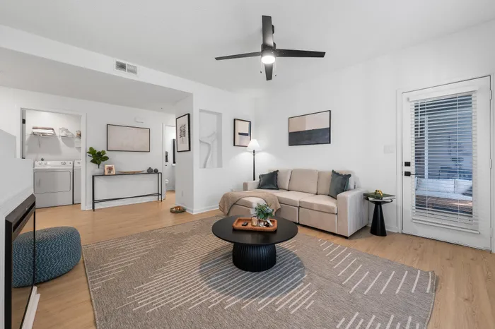 Bright and modern living room featuring a cozy beige sofa, chic coffee table, and stylish wall art, with a view into a functional laundry area.