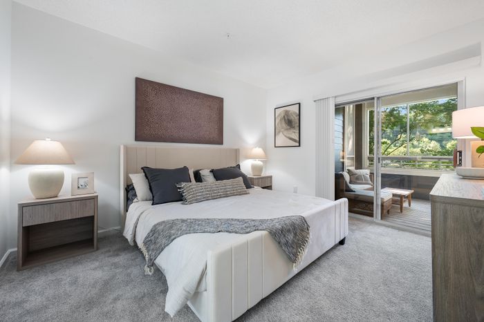 Elegant bedroom with modern decor, featuring a plush bed, accent artwork, and a serene view through glass sliding doors leading to a cozy balcony.