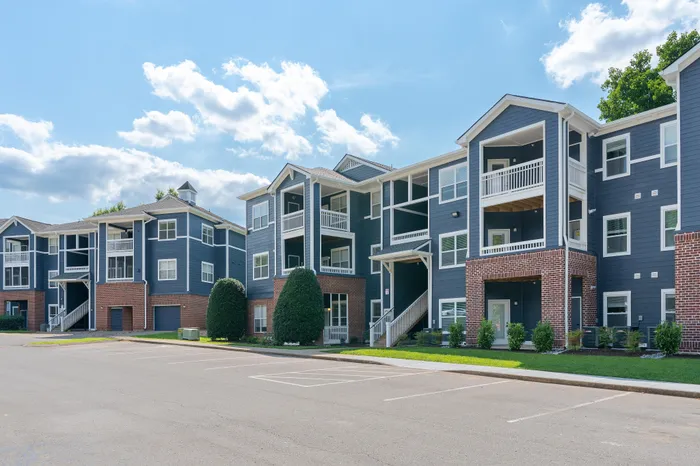 Modern apartment complex with stylish blue and brick exterior, featuring spacious balconies and well-maintained landscaping under a bright blue sky.