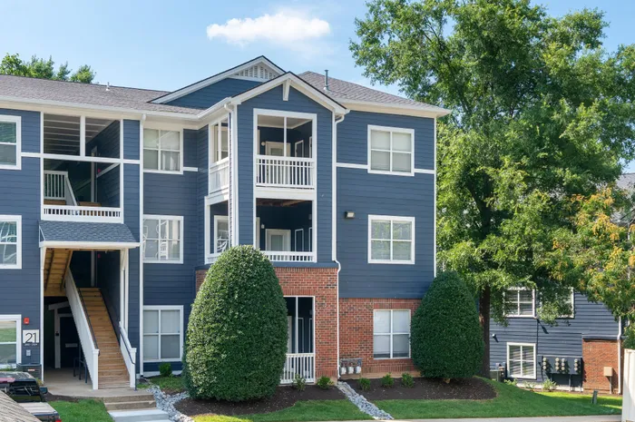 Charming apartment complex with modern blue siding, white trim, and inviting balconies amidst lush greenery.