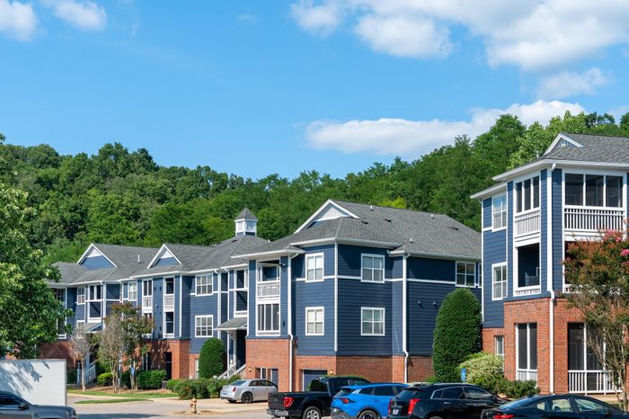Charming apartment complex with elegant blue siding and brick accents, nestled amidst lush greenery and clear skies.