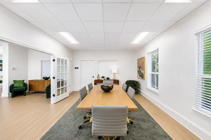 Elegant conference room with a long wooden table, stylish gray chairs, chic decor, and ample natural light through large windows.