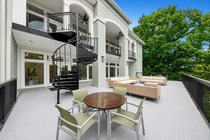 Elegant outdoor patio with stylish spiral staircase and modern seating, surrounded by lush greenery and expansive windows.