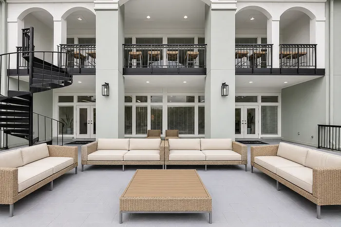 Elegant outdoor lounge area with modern wicker sofas and central table, set against a stylish building facade with upper balcony and spiral staircase.