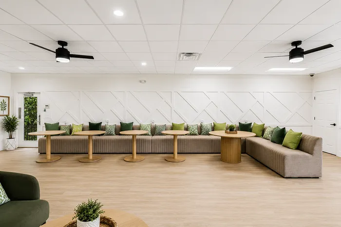 Elegant lounge area featuring modern beige seating, wooden tables, and vibrant green accent pillows against a textured white wall.