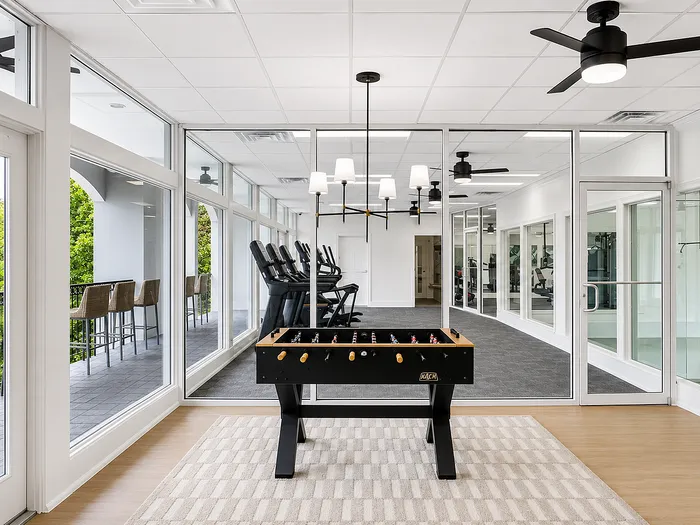 Modern recreational area with foosball table, large windows, and a stylish gym setup offering a scenic view.