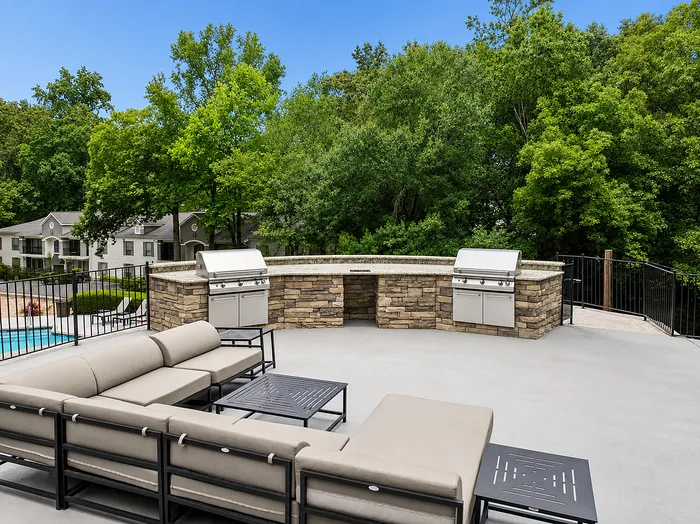 Chic outdoor patio featuring elegant stone BBQ area with modern grills, surrounded by lush greenery.