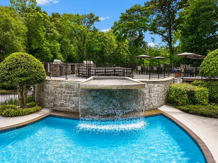 Luxurious outdoor pool with cascading waterfall, surrounded by lush greenery and elegant patio seating.