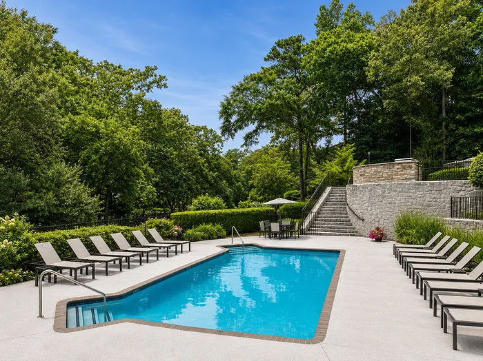 Inviting outdoor pool surrounded by lush greenery and stylish lounge chairs, offering a serene escape under a clear blue sky.