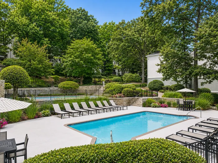 Lush apartment complex pool area with inviting lounge chairs and vibrant greenery, offering a serene outdoor retreat.