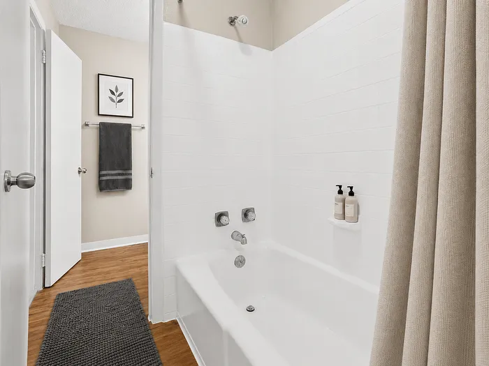 Elegant bathroom featuring a pristine white bathtub, modern fixtures, and cozy wooden flooring, complemented by tasteful wall art and sleek towel accents.