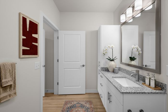 Bright and modern bathroom with sleek granite countertops, elegant lighting fixtures, and stylish white cabinetry, featuring a decorative plant and contemporary artwork for a touch of sophistication.