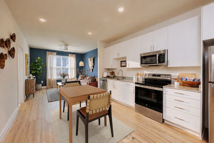 Elegant open-plan apartment kitchen and living area featuring sleek white cabinetry, modern appliances, a cozy dining space, and ample natural light.