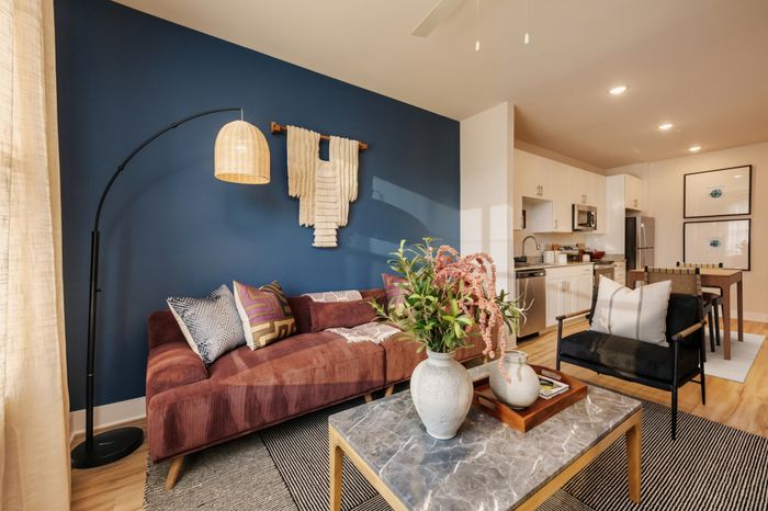 Chic and inviting living area with a modern sofa, striking blue accent wall, and stylish open-concept kitchen.