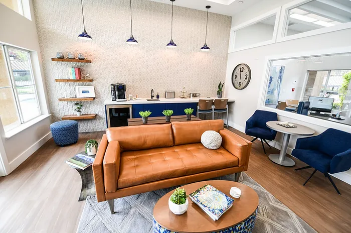 Chic apartment lounge with a modern leather sofa, vibrant blue chairs, and a sleek coffee bar, creating a welcoming and stylish ambiance.