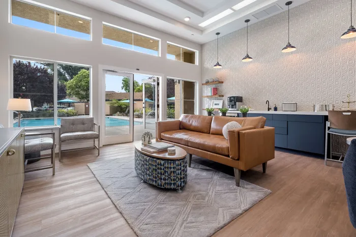 Modern living area with elegant decor, featuring a sleek leather sofa, chic lighting, and large windows offering a poolside view.
