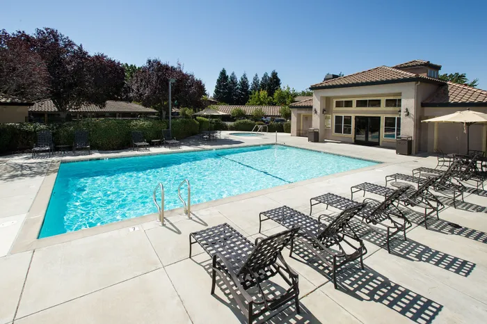 Inviting outdoor swimming pool with stylish lounge chairs and modern clubhouse backdrop, surrounded by lush greenery and serene ambiance.