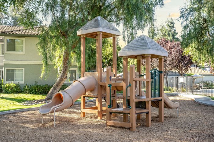 Charming playground area with engaging slides and climbing structures, surrounded by lush greenery and residential homes.