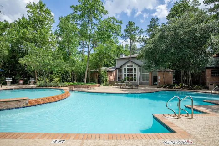 Inviting outdoor pool area surrounded by lush greenery and a modern clubhouse, perfect for relaxation and entertaining.