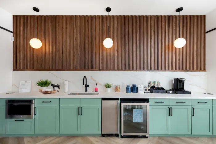 Sleek modern kitchenette showcasing mint green cabinets, marble countertops, and warm wood paneling with elegant lighting.