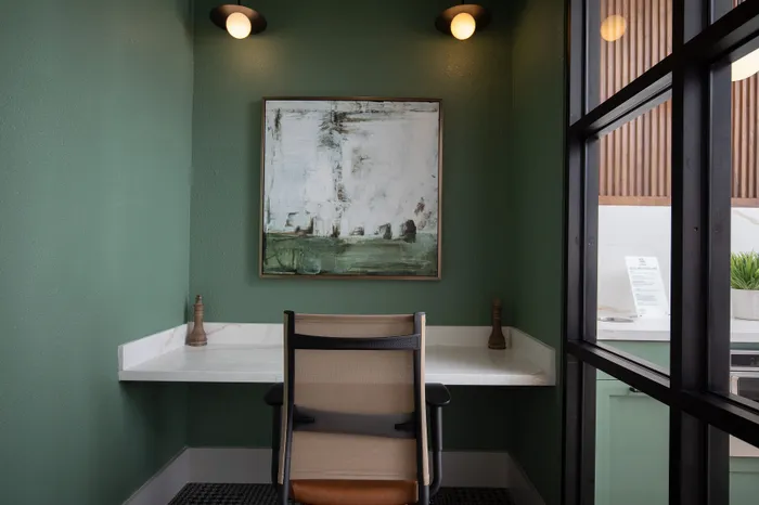 Chic home office space with elegant green walls, modern lighting, and abstract art creating a serene work environment.