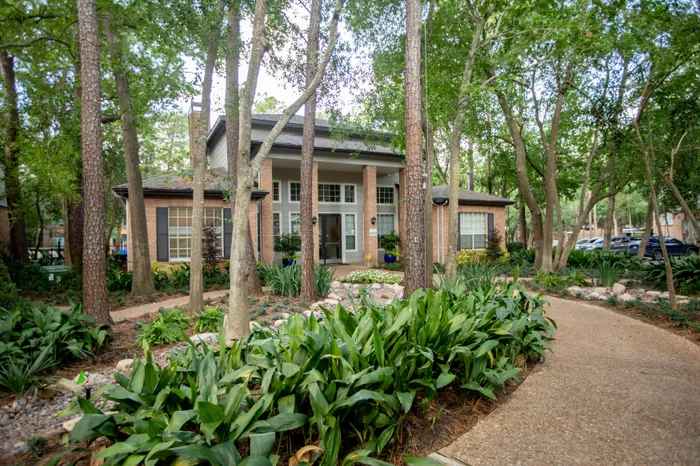 Charming brick Resident Clubhouse nestled among lush greenery, featuring large windows and a welcoming entrance.