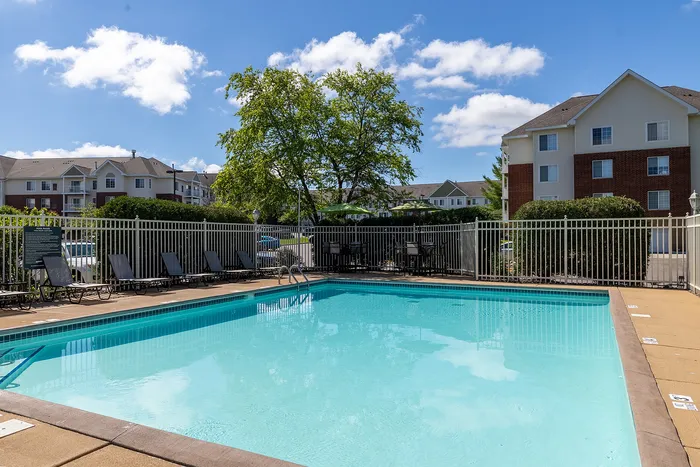 Inviting outdoor pool with lounge chairs, surrounded by a well-maintained fence and lush greenery, perfect for relaxation and leisure in a modern apartment community.