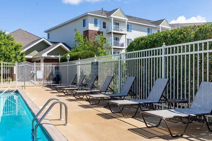 Inviting apartment complex with a sunlit outdoor pool area lined with modern lounge chairs, perfect for relaxation.
