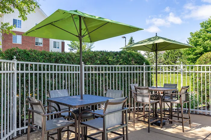 Charming outdoor patio with green umbrellas, elegant seating, and lush garden view, perfect for relaxation and social gatherings.