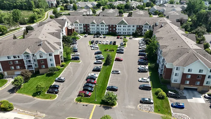 Aerial view of a modern apartment complex with spacious parking, lush greenery, and well-maintained surroundings.