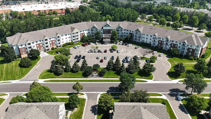Aerial view of a beautiful apartment complex with charming architecture, surrounded by lush greenery and ample parking space, offering a serene residential setting.