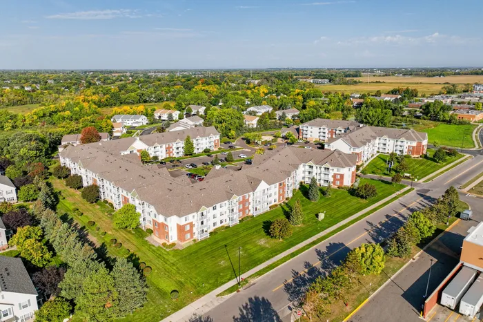 Aerial view of a charming suburban apartment complex surrounded by lush greenery and wide open spaces, offering a peaceful lifestyle.