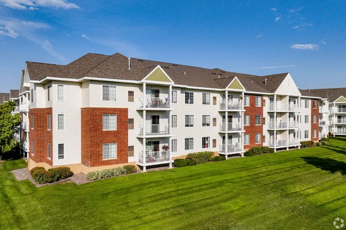 Charming apartment complex showcasing classic brick and siding exterior with spacious balconies, surrounded by lush green lawns under a clear blue sky.