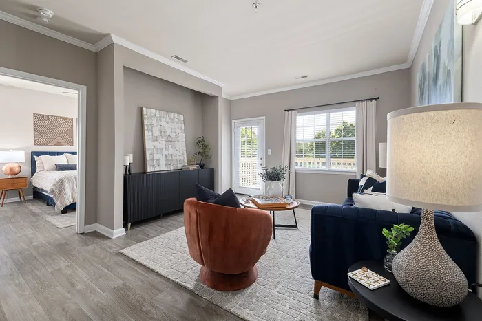 Chic living room with modern decor, featuring a plush rust armchair, elegant sofa, and sleek wooden flooring, leading into a cozy bedroom with stylish accents.
