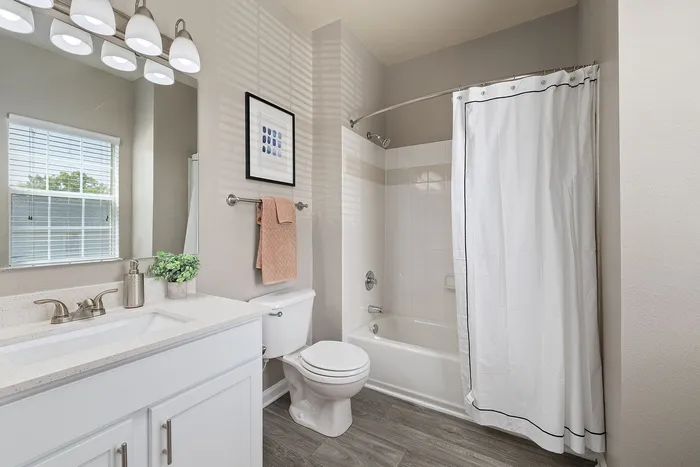 Elegant bathroom with sleek white cabinetry, modern fixtures, and a spacious bathtub, enhanced by natural light through a large window.