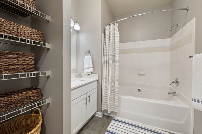Elegant bathroom featuring a modern white vanity, relaxing bathtub with stylish shower curtain, and organized shelving with woven baskets.