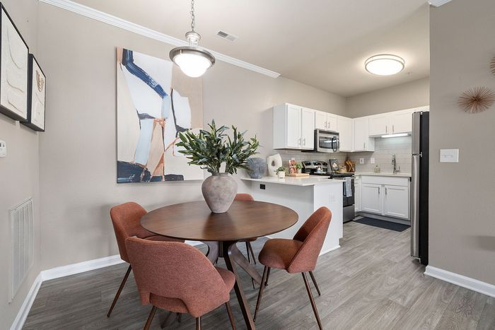 Modern dining area with stylish round table and elegant chairs, complemented by sleek kitchen with stainless steel appliances and contemporary art.