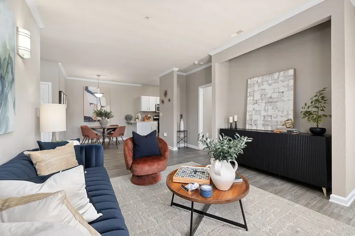 Elegant living room with stylish decor, featuring a plush navy sofa, cozy red chair, and modern dining area leading to a chic kitchen.